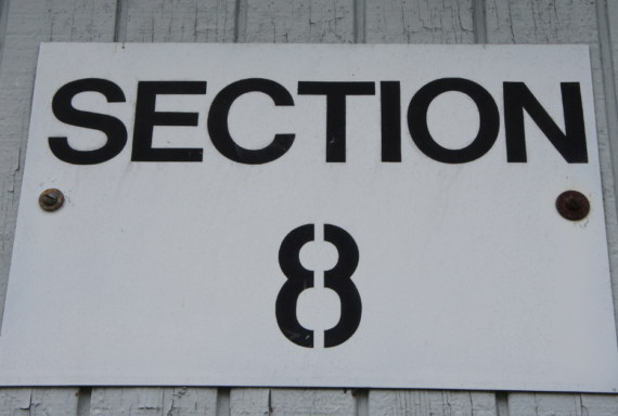 Property Management White sign labeled 'Section 8' mounted on a wall, referencing a federal housing assistance program for low-income renters